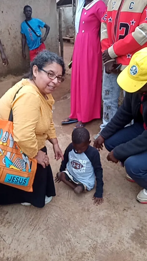 Una voluntaria de Dorcas Foundation arrodillada junto a un niño durante una visita comunitaria.