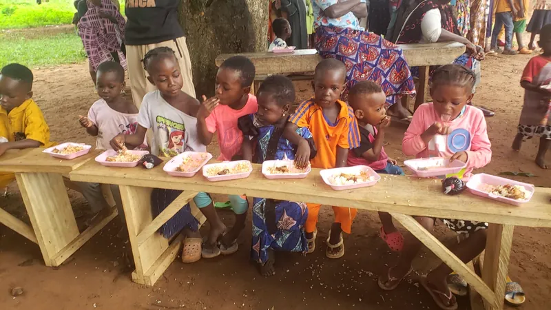 Niños sentados a una mesa larga de madera comiendo juntos en un evento comunitario de Dorcas Foundation.