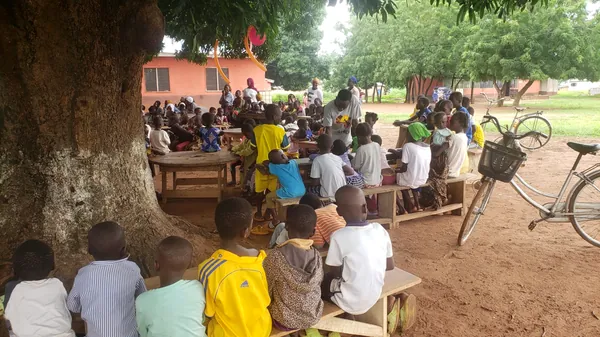 Niños y adultos reunidos bajo un árbol para un evento comunitario.